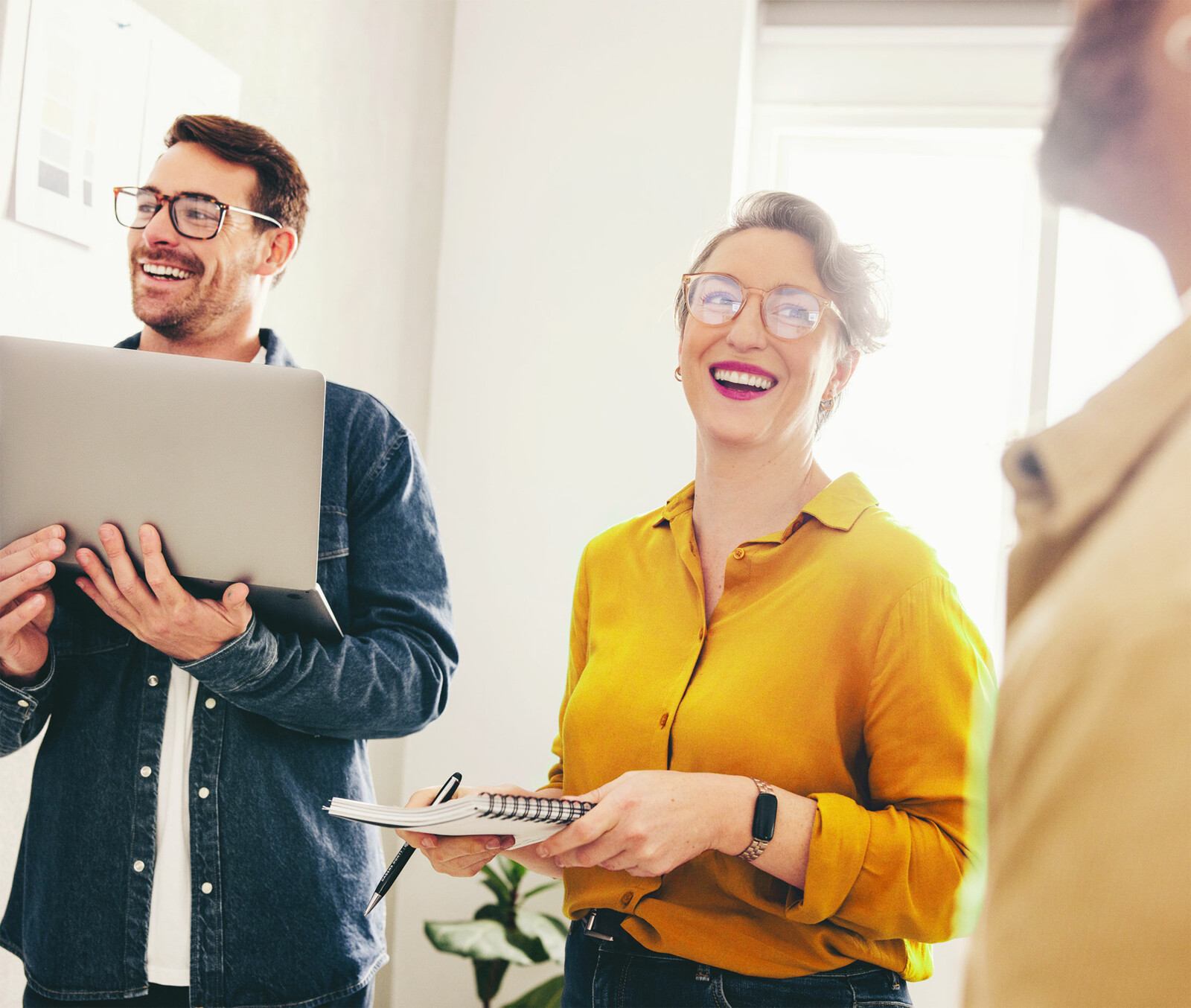 Lächelnde Teammitglieder bei einer Besprechung, eine Person hält ein Notebook