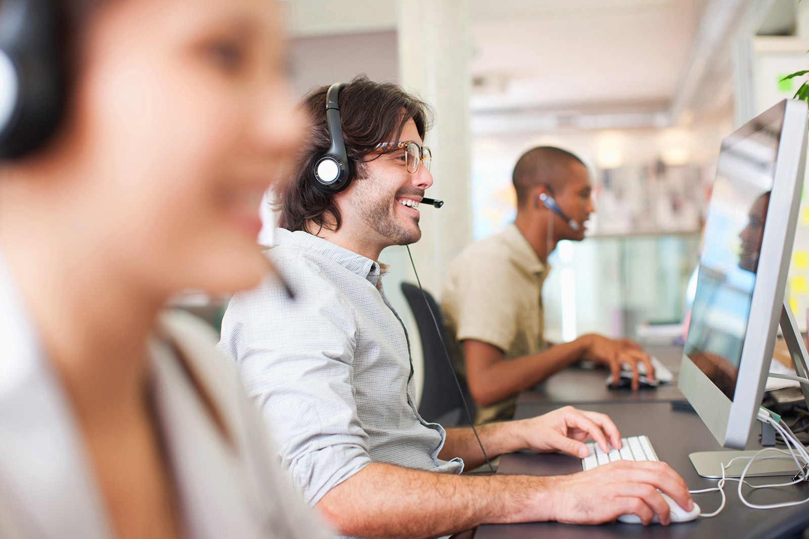 Drei Mitarbeitende mit Headsets arbeiten an Computern in einem Büro