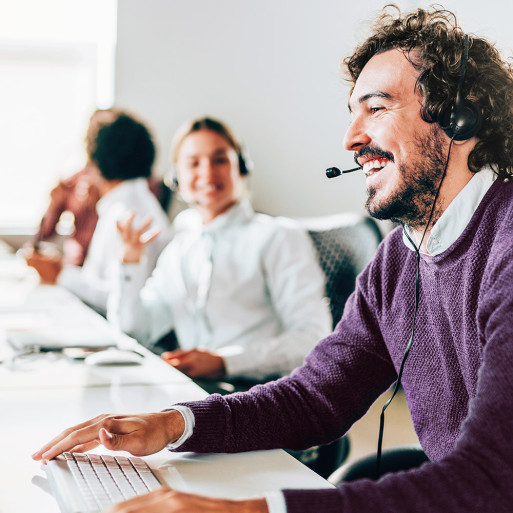 Mitarbeitende mit Headsets arbeiten lächelnd am Schreibtisch