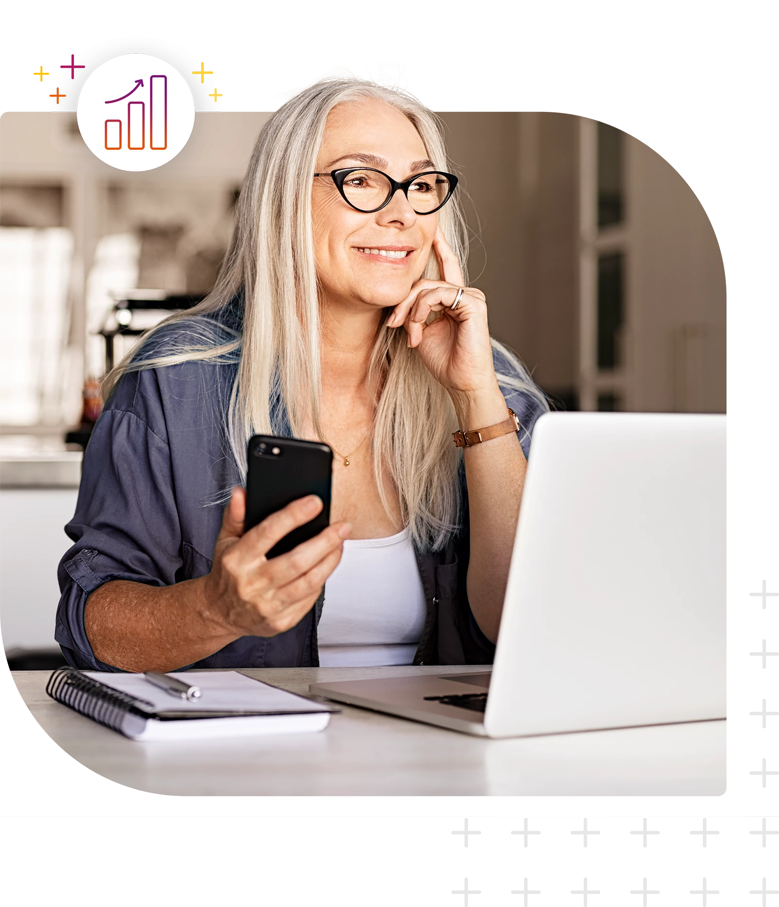 Person sitzt an einem Schreibtisch mit Laptop, Smartphone und Notizbuch.